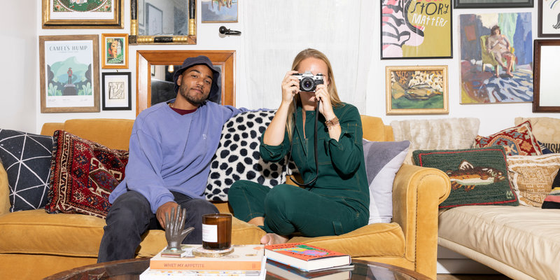 man and woman sitting on a yellow sofa while the woman is holding up a camera