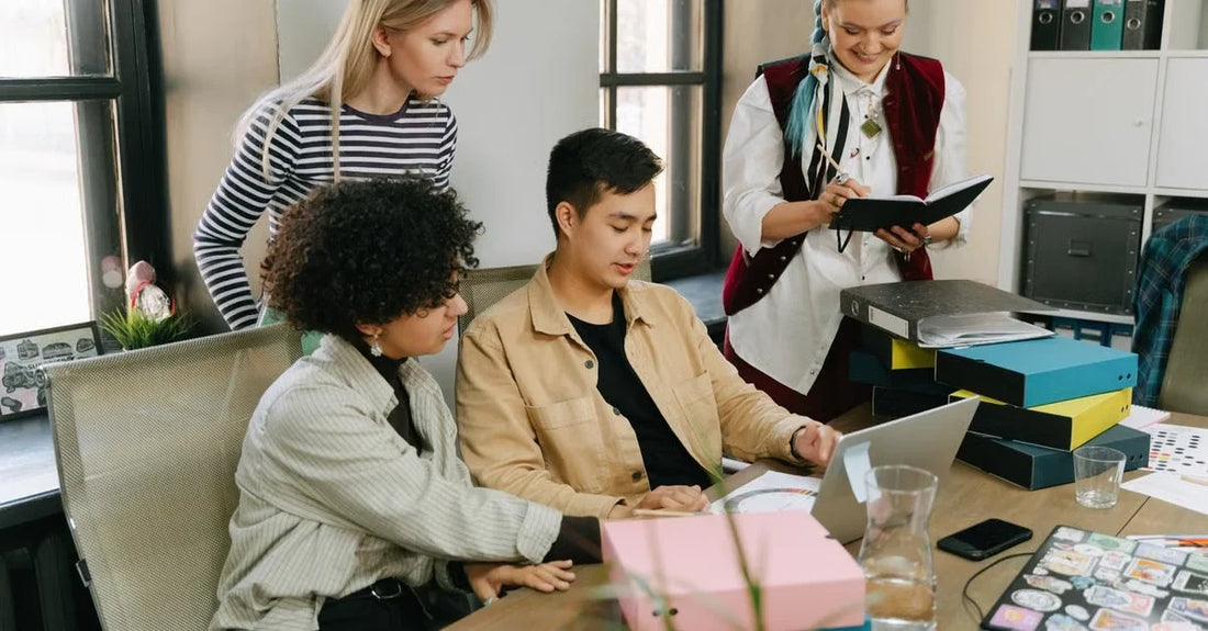 Four colleagues collaborating on digital marketing small business strategy at desk with notebooks and materials.