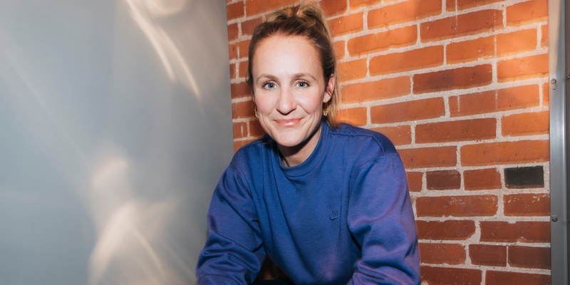 woman in a blue shirt smiling with a brick wall in the background