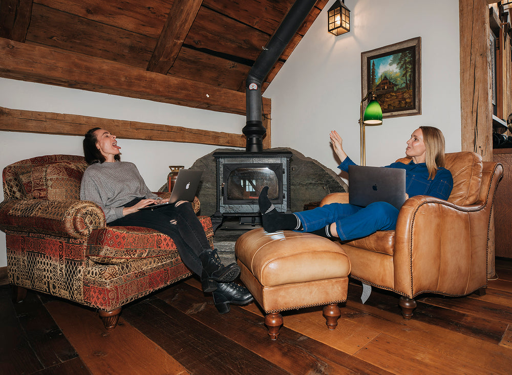 Founder of Strong Brand Social, Katie Wight, and Social Media Guru, Caitlin Bergin, sitting in armchairs with their laptops in a cozy loft, tossing popcorn into each other's mouth.